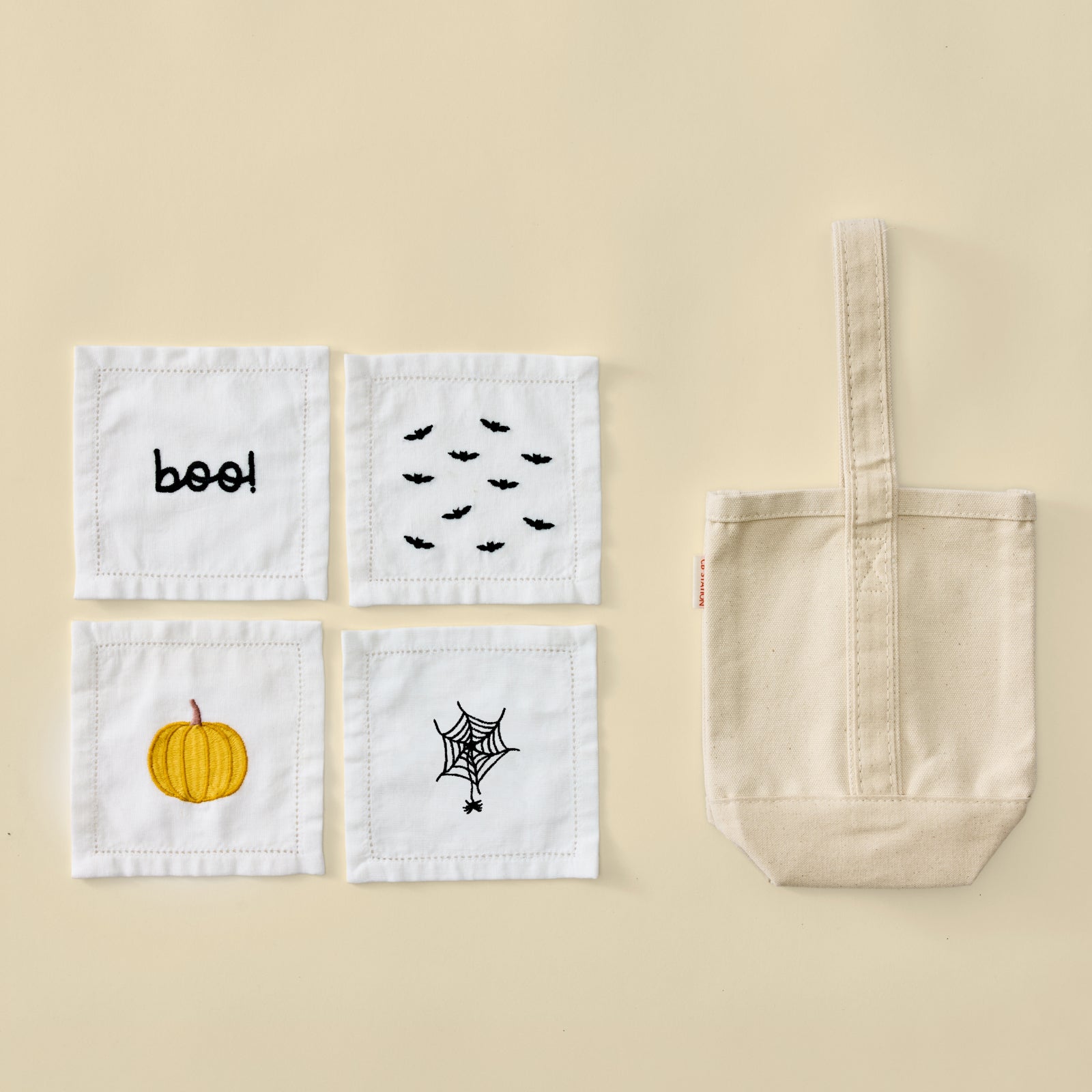 Plain cream canvas wine tote bag next to four white Halloween embroidered cocktail napkins.