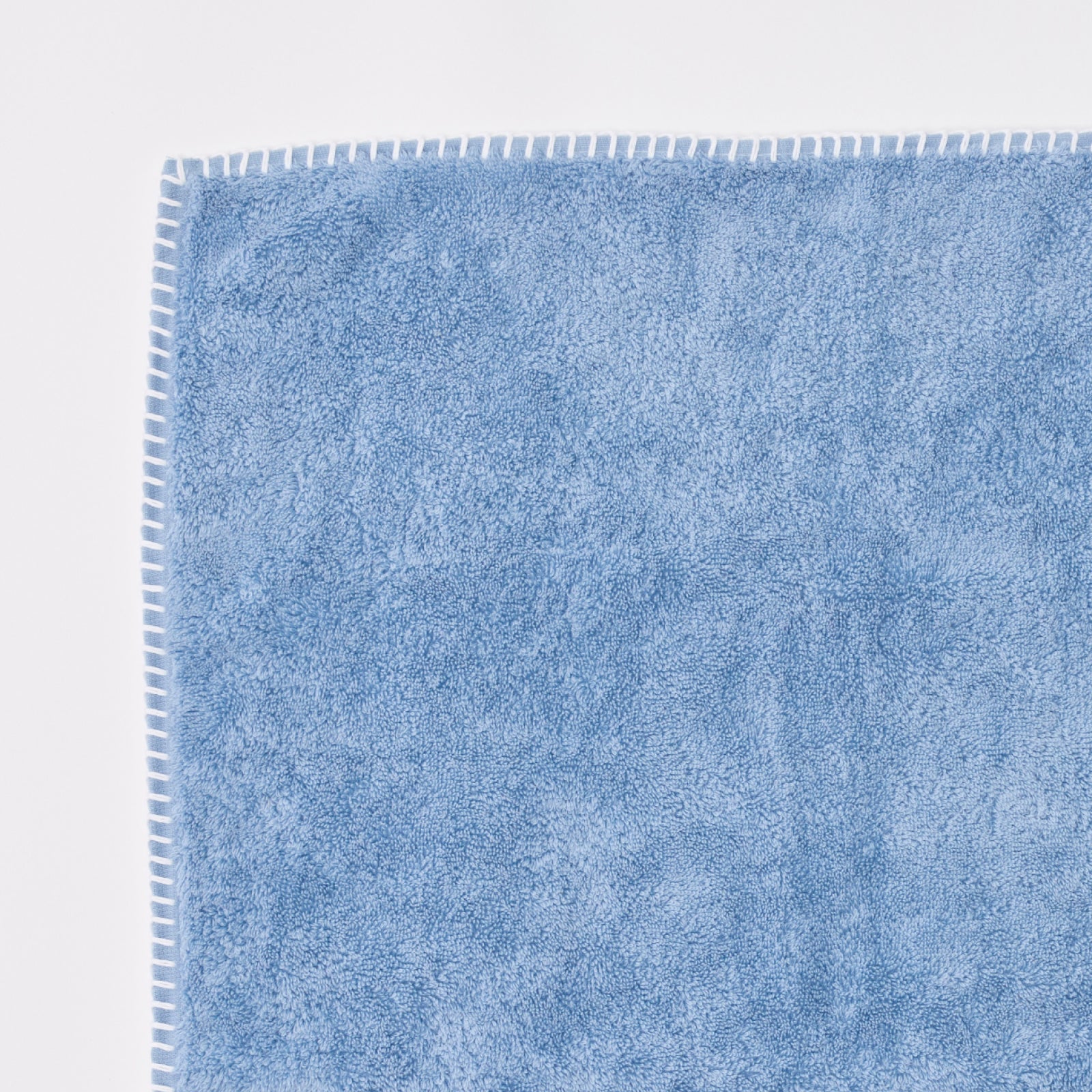 Stitched Edge Hand Towels in Storm Blue, a blue towel corner with white blanket-stitch edging.