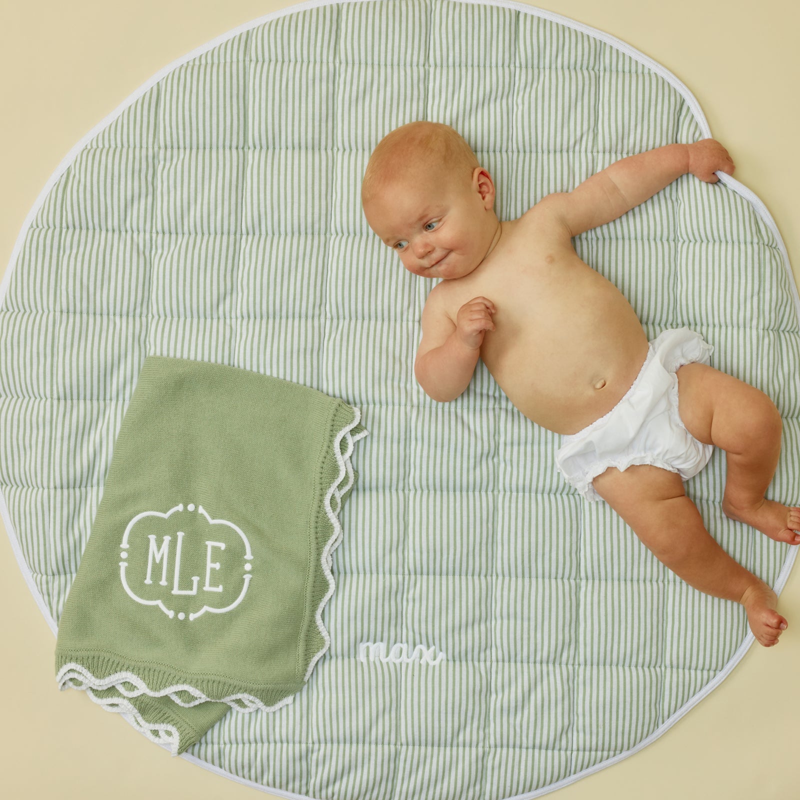 Baby on the sage striped tummy time mat beside the knit blanket with a sample monogram