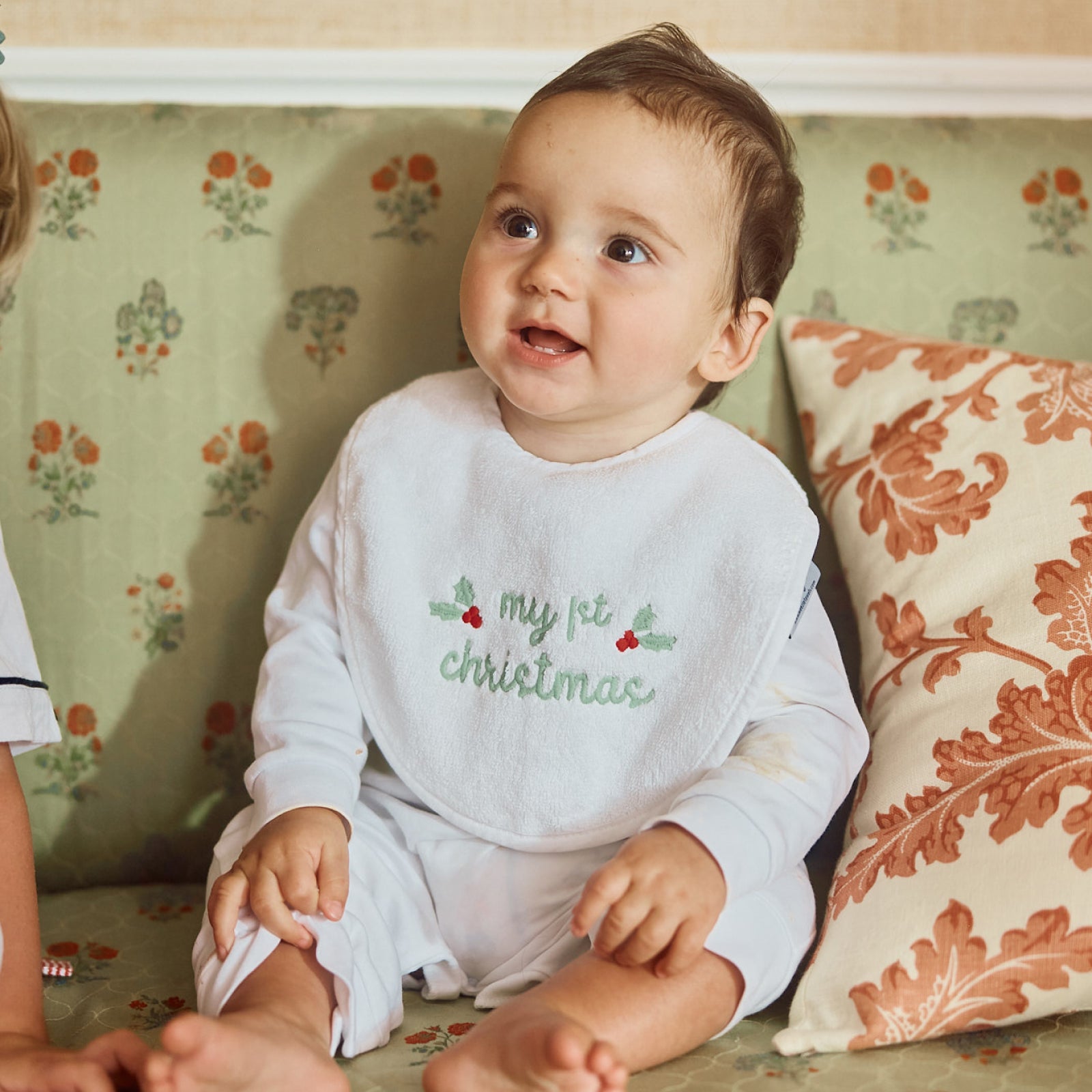 Baby wearing the My First Christmas bib, seated on a sofa