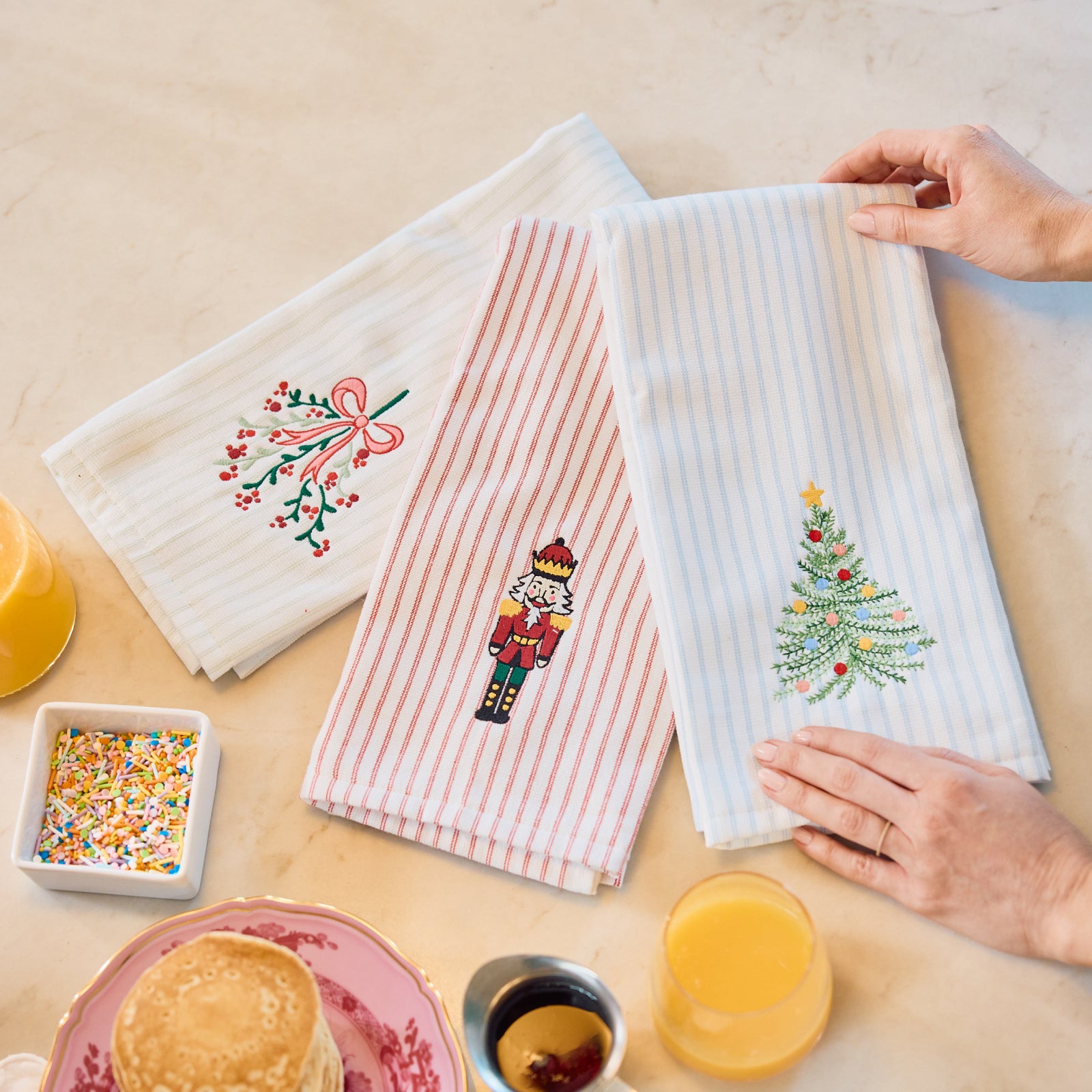 Holiday Hosting Set in Tidings Trio, striped towels with mistletoe, nutcracker and tree embroidery on a brunch table