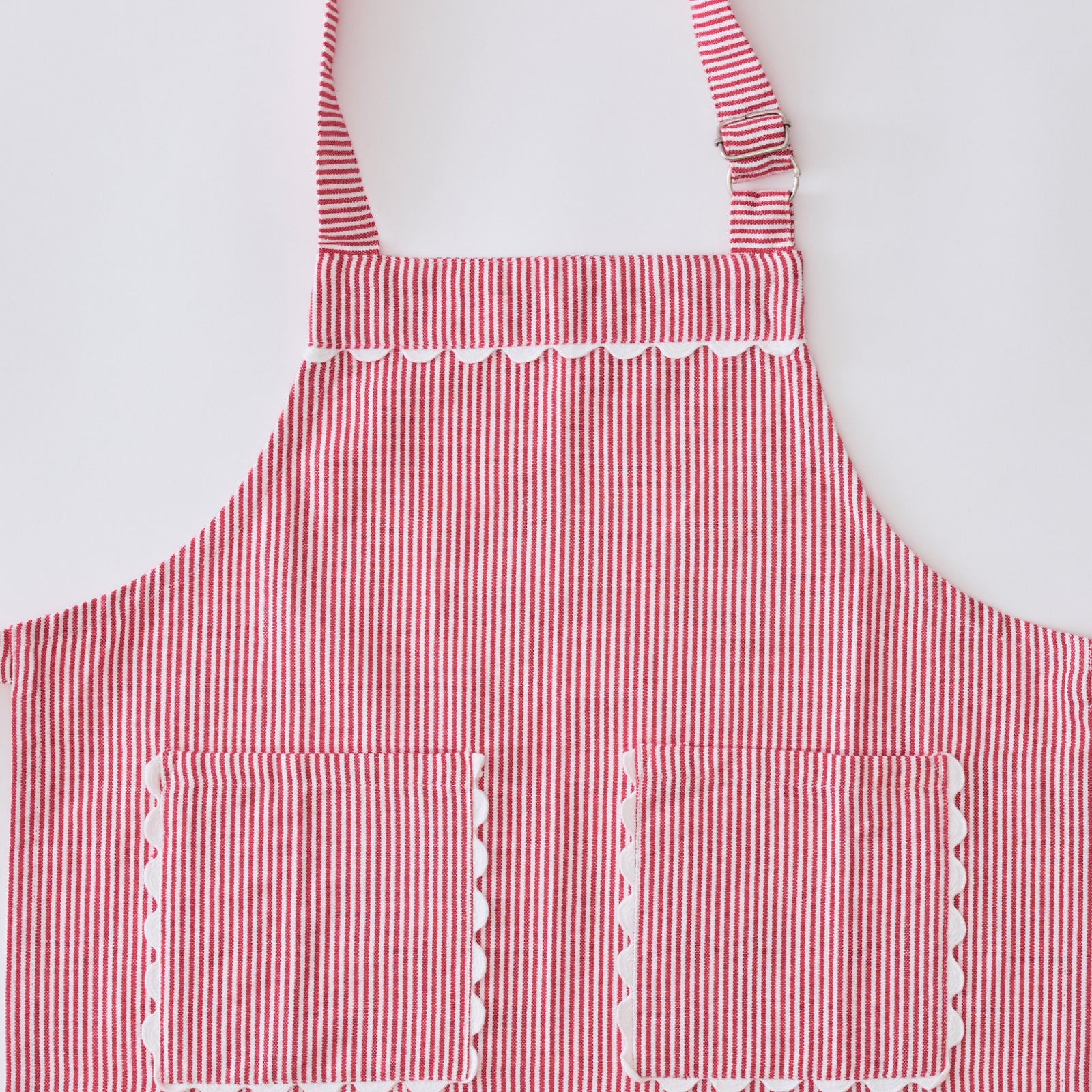 A red and white striped apron with two front pockets and scalloped trim, shown against a plain white background.