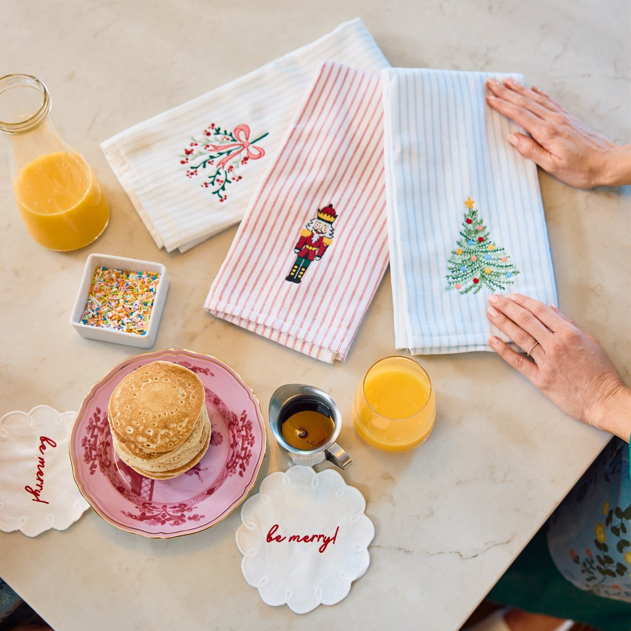 Striped hand towels embroidered with a Christmas tree, nutcracker and mistletoe bow on a breakfast table.