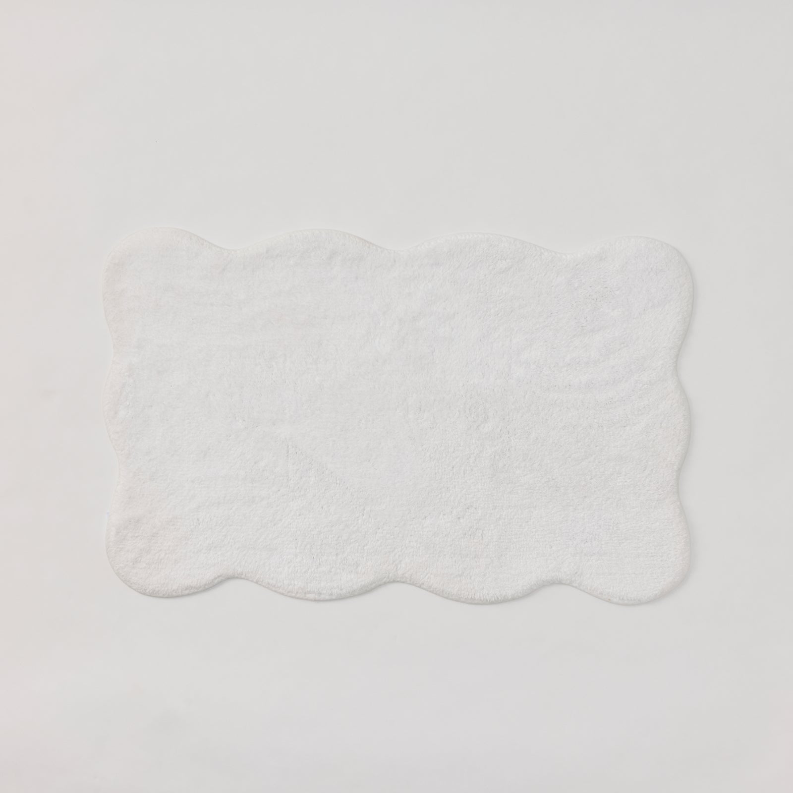 A plush white bath rug with scalloped edges.