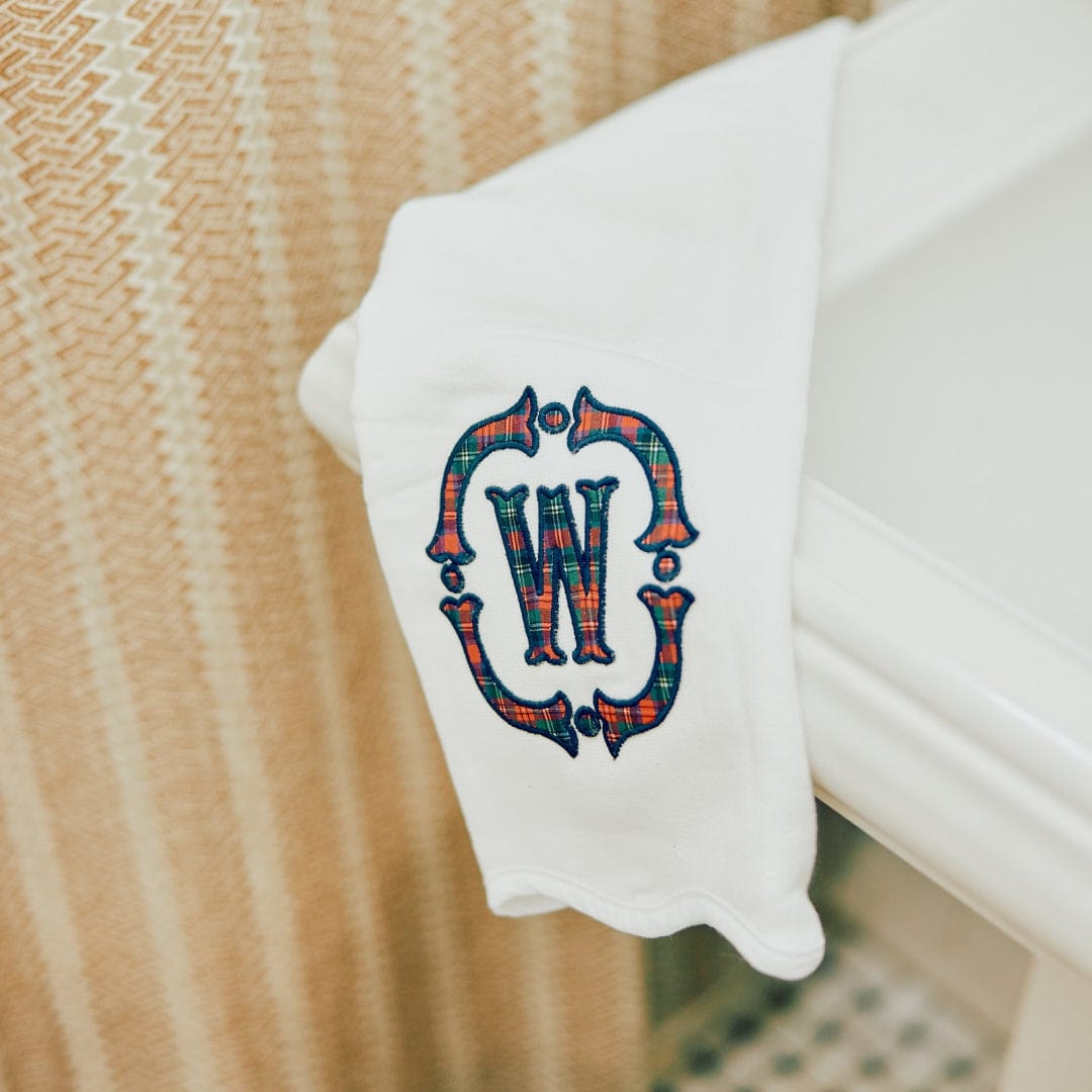 White powder bath towel with a Tartan plaid appliqué crest monogram "W" draped over the edge of a white bathtub