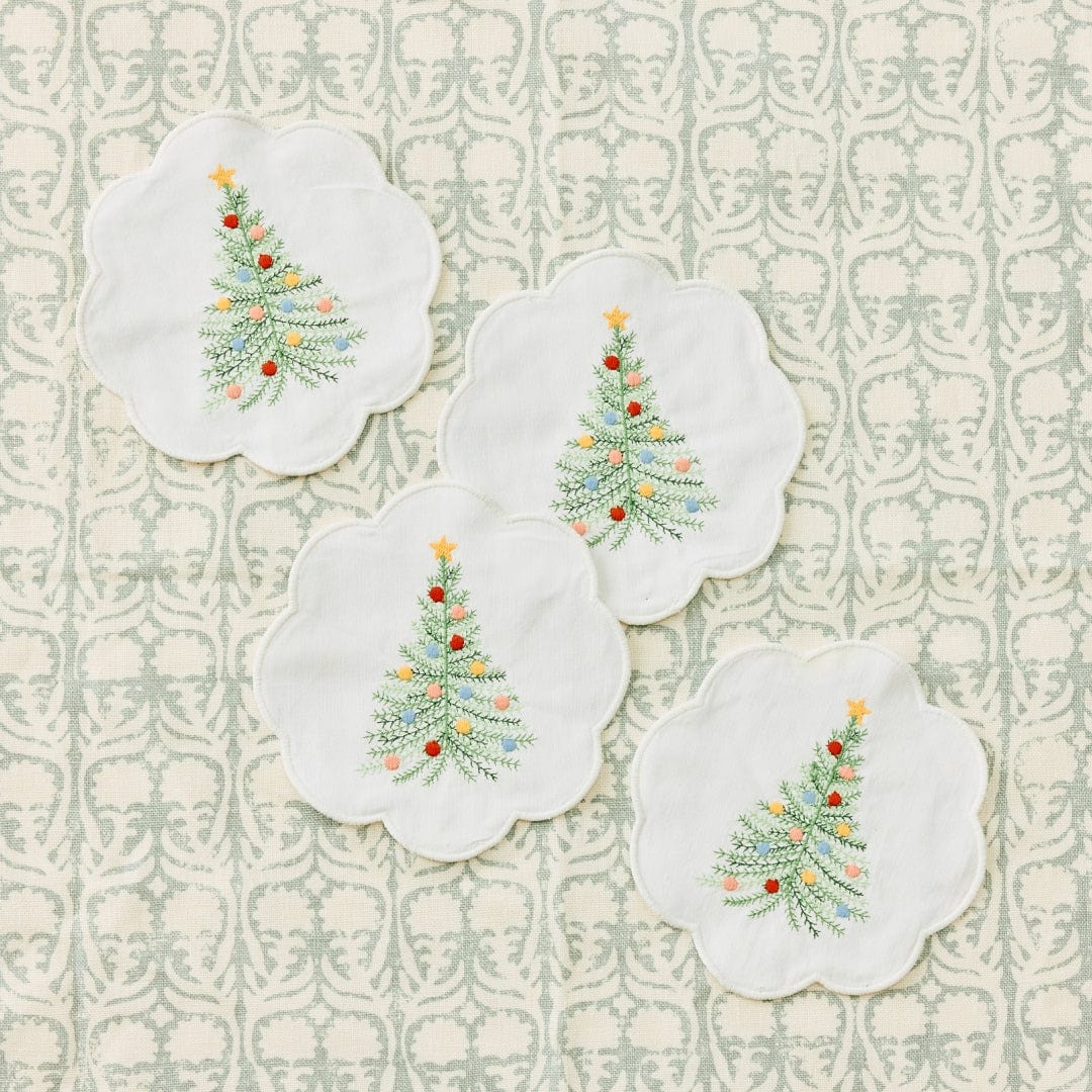 Four white Holiday Tree cocktail napkins embroidered with a green tree, colorful ornaments, and gold star on a sage print