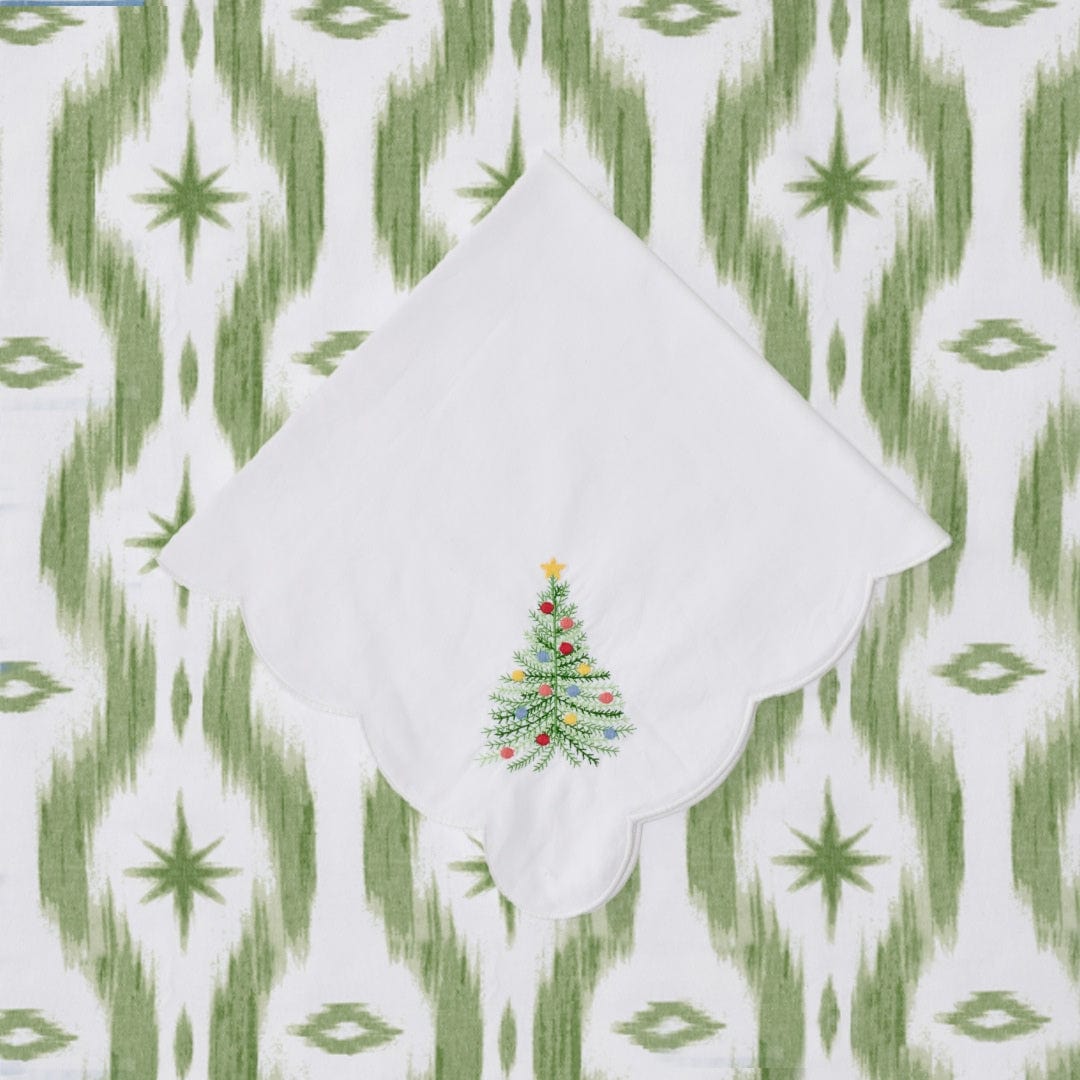 White Holiday Tree dinner napkin folded into a point, with an embroidered ornament-trimmed tree, on a green ikat cloth