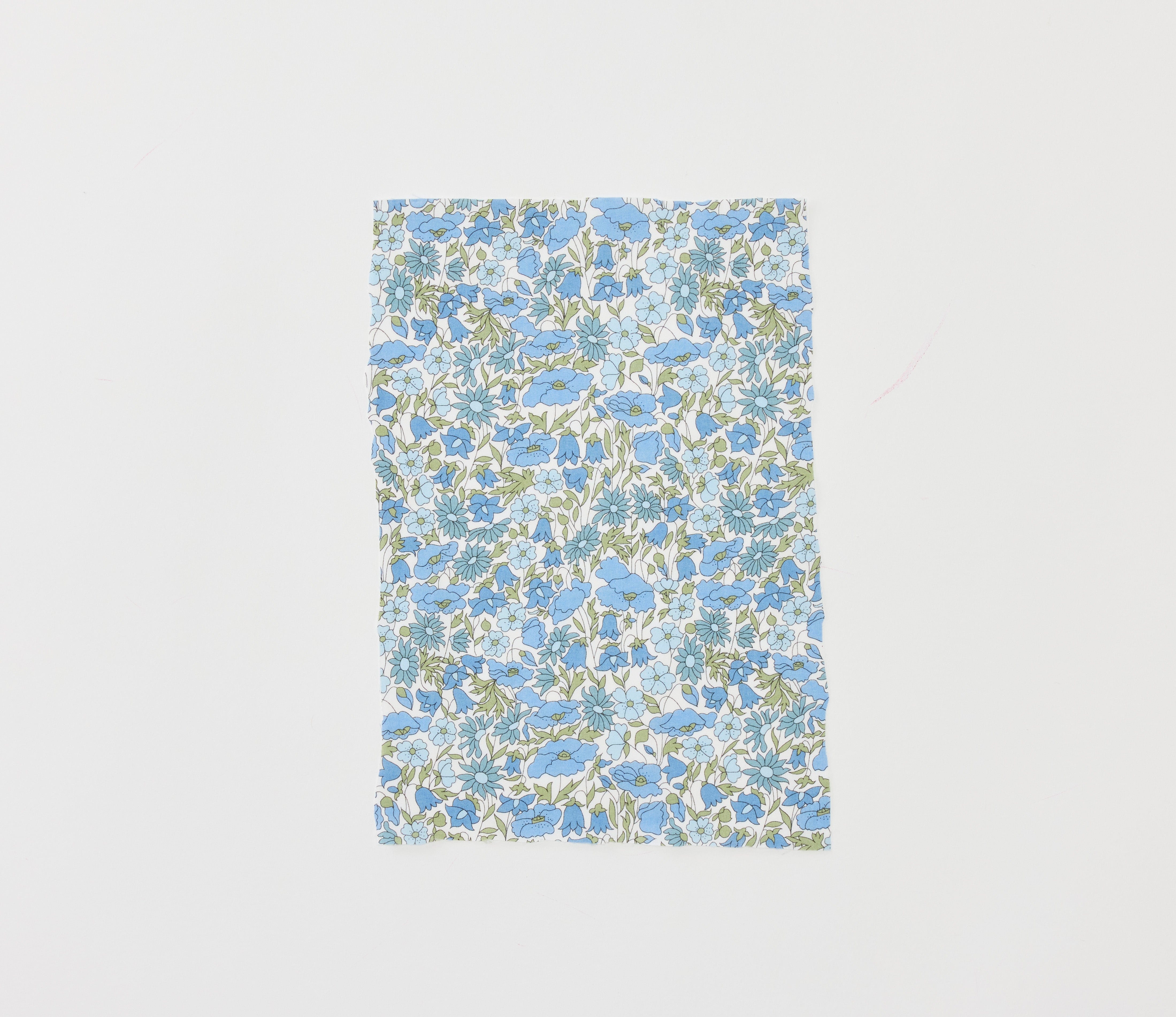 Swatch of the blue and green Liberty floral fabric used for the Liberty Blue Heart appliqué, laid flat on light gray
