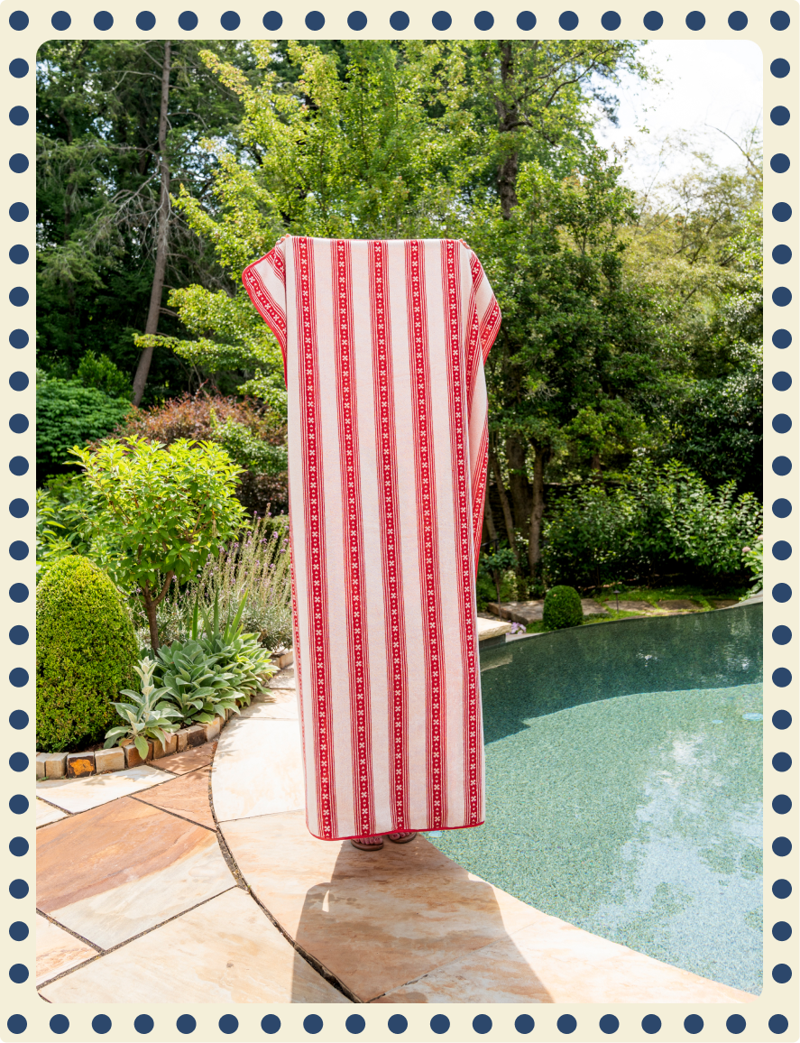 Red and white striped towel draped over a chair by a pool with greenery in the background