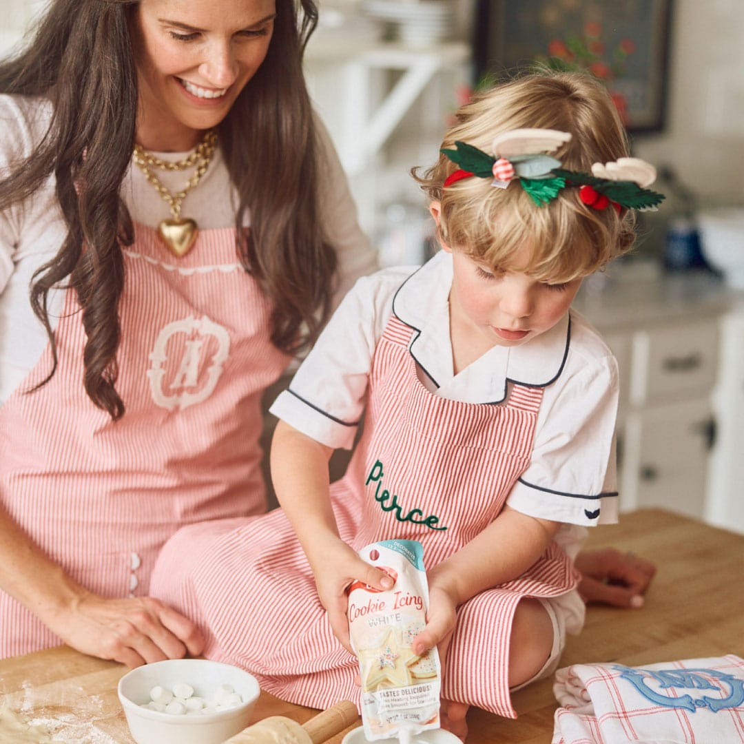 A woman and a child in monogrammed red striped aprons baking together.
