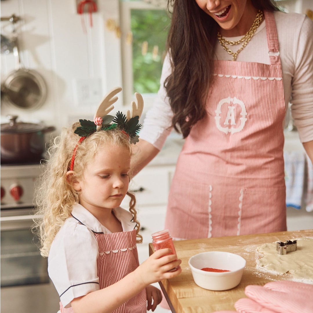 A woman in a monogrammed red striped apron baking with a child at a kitchen counter.