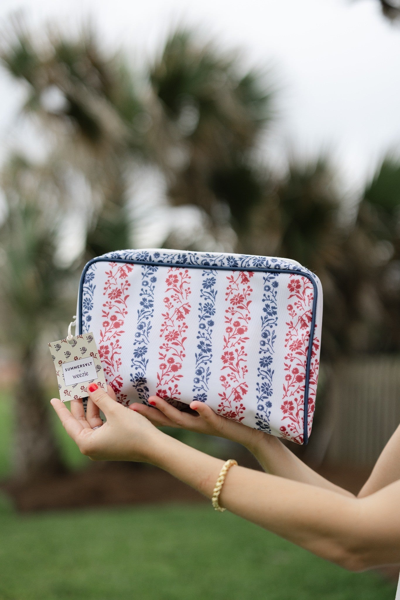Person holding a floral-patterned pouch with a blurred natural background