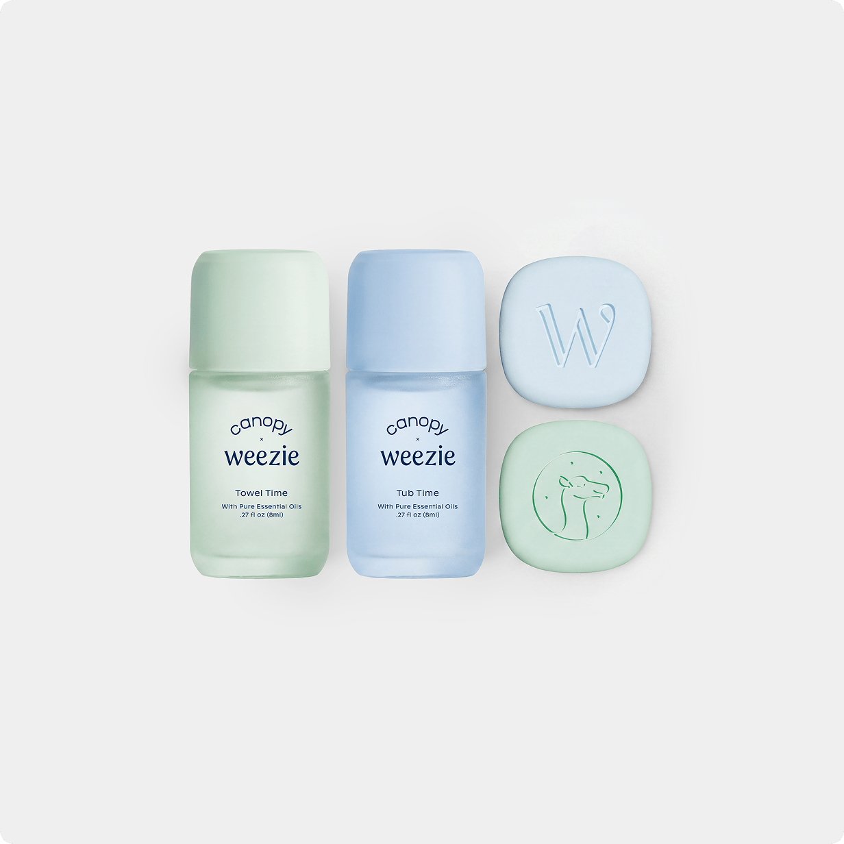 Three Weezie skincare items arranged on a light gray background: a mint green Travel Time bottle, a light blue Tub Time bottle, and two matching round bars, one embossed with a W and the other with a face outline.